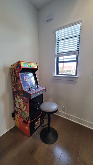 A gaming arcade machine in a room with a window and a wooden floor. - Downtown Entertainer's Oasis (San Antonio)