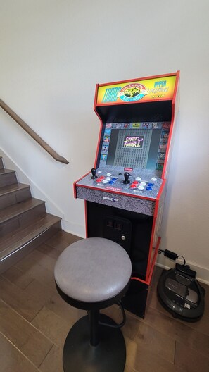 A gaming arcade machine with a stool in front, located near a staircase. - Downtown Entertainer's Oasis (San Antonio)
