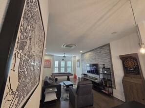 A modern living room with a pool table, comfortable seating, a flat-screen TV, and a dartboard. - Downtown Entertainer's Oasis (San Antonio)