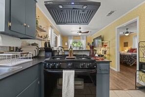Una cocina con estufa central, ventilador de techo y vistas al dormitorio contiguo.
