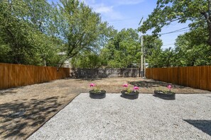 A backyard with a gravel patio, wooden fence, and three planters with pink flamingos. - The Sundown - Freshly Renovated, Cozy North Loop Home w/ Hot Tub (Austin)
