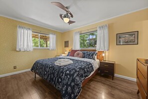A bedroom with a bed, nightstands, a dresser, a ceiling fan, and two windows with curtains. - The Sundown - Freshly Renovated, Cozy North Loop Home w/ Hot Tub (Austin)