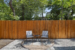 A fenced outdoor area with two metal chairs and a small table, surrounded by gravel. - The Sundown - Freshly Renovated, Cozy North Loop Home w/ Hot Tub (Austin)