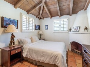 Ein Schlafzimmer mit Holzboden, einem Bett, einem Nachttisch, einer Lampe, einem Kamin und einer Wand mit Bildern.