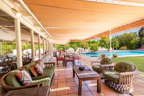 An outdoor patio area with a covered seating arrangement, a pool, and a view of the surrounding greenery. - San Jacinto Villa - 5BD | Pool | Movie Colony (Palm Springs)