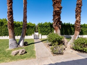 A pathway leading to a gated entrance, surrounded by palm trees and a hedge. - San Jacinto Villa - 5BD | Pool | Movie Colony (Palm Springs)