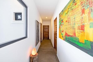 Un couloir au design moderne, orné d’un grand tableau abstrait sur le mur de droite, d’une photographie encadrée sur le mur de gauche et d’une petite table avec une lampe sur le côté gauche.