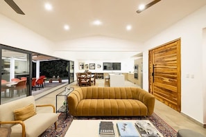 A modern living room with a sofa, coffee table, and a dining area in the background. - 5 Bedroom Villa in Hacienda Pinilla Golf Resort (Hacienda Pinilla)