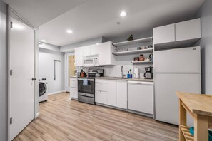 A modern kitchen with white cabinetry, stainless steel appliances, and a wooden floor. - Avenue Nook | Pet Friendly | Grill | Desk (Salt Lake City)