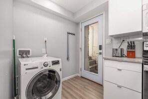 A laundry room with a front-loading washing machine, a drying rack, and a small kitchen area with a toaster and knives. - Avenue Nook | Pet Friendly | Grill | Desk (Salt Lake City)