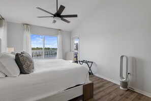 Ein Schlafzimmer mit Bett, Deckenventilator, Fenster mit Blick auf das Wasser und einem Standheizkörper.