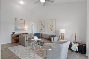 A modern living room with a sofa, a coffee table, and a rug. There are framed artworks on the wall and a guitar in the corner. - Fully Remodeled "Coastal Luxe" with 1 mile of amazing River Views. Unmatched!! (Crystal River)