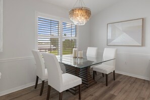 A dining area with a glass table, white chairs, a chandelier, and a view through large windows. - Fully Remodeled "Coastal Luxe" with 1 mile of amazing River Views. Unmatched!! (Crystal River)