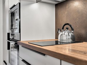 A kitchen with a stainless steel kettle on a wooden countertop, a built-in oven, and a microwave. - Mánesova by Interhome (Jachymov)