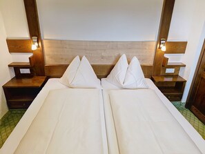 A double bed with two pillows, wooden headboard, bedside tables with lamps, and a green patterned floor. - Ferienhaus Brigitte by Interhome (Längenfeld)