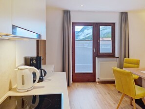 A compact kitchen with a coffee maker, a kettle, and a microwave. There is a dining area with a table and chairs, and a window with a view of mountains. - Ferienhaus Brigitte by Interhome (Längenfeld)