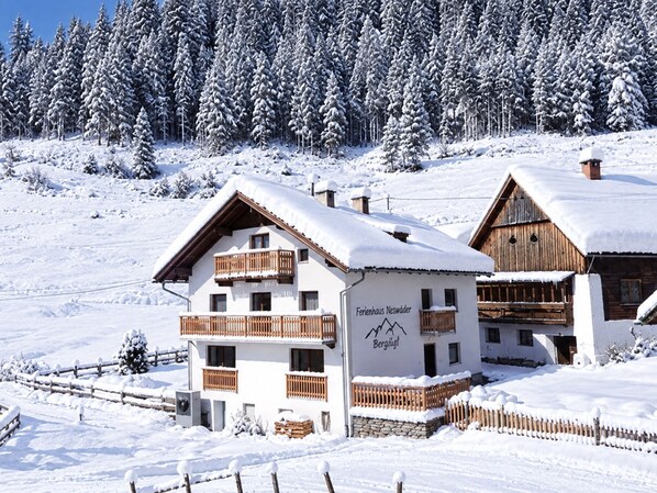 Edificio cubierto de nieve con un balcón y un cartel que dice 'Ferienhaus Neskawer Bergliust'.