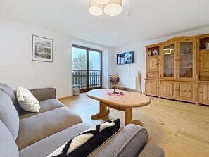 Un salon comprenant un canapé, une table ronde en bois, un téléviseur et un meuble en bois.