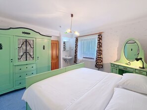 Un dormitorio con cama, armario, espejo y ventana con cortinas.