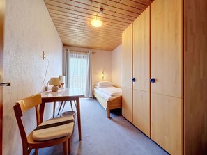 A small, cozy room with a bed, a desk, and a chair. There is a window with curtains, a ceiling light, and a wall-mounted heater. - Dösentaler Bergidyll by Interhome (Mallnitz)
