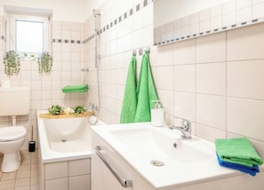 Ein Badezimmer mit Toilette, Waschbecken und Badewanne. Grüne Handtücher hängen an der Wand.