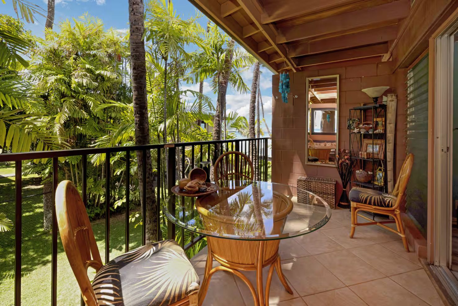 A balcony with a glass table, wicker chairs, and a view of palm trees.