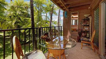 A balcony with a glass table, wicker chairs, and a view of palm trees.
