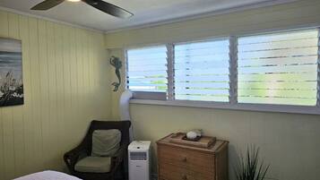 A bedroom with a bed, a chair, a dresser, a ceiling fan, and a window with blinds.