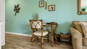 A room with a green wall, a wooden floor, a wicker chair, a small table, a wicker basket, and a beige sofa.
