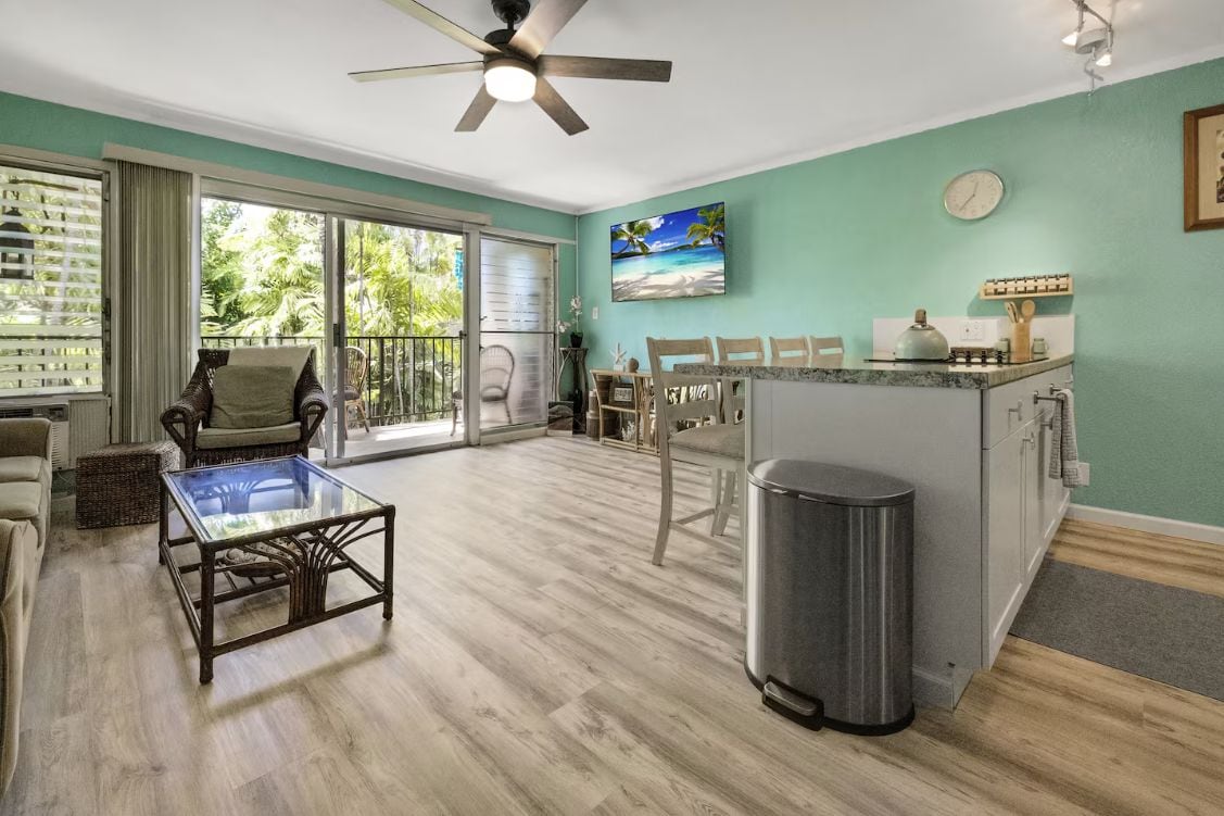 A spacious living area with a glass coffee table, a ceiling fan, and a kitchen area with a sink and countertop.