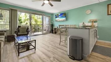 A spacious living area with a glass coffee table, a ceiling fan, and a kitchen area with a sink and countertop.