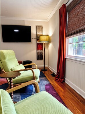 Een woonkamer met een flatscreen televisie, een vloerlamp, een bank en een raam met gordijnen.
