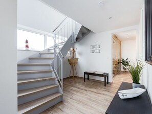 Un interior modern amb una escala, una banca, un senyal de paret i una planta en test.
