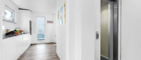 A modern kitchen with white cabinets, a wooden floor, and a view through a door.