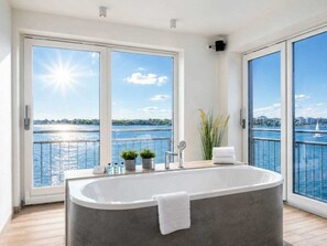 A modern bathroom with a freestanding bathtub, large windows, and a view of a body of water. - Holiday Apartment With 1 Bedroom (Kappeln)