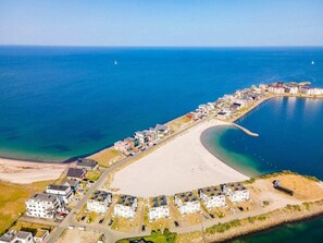 Vista aèria d'una zona costanera amb una platja sorrenca, una marina i una filera d'edificis blancs al llarg de la riba.