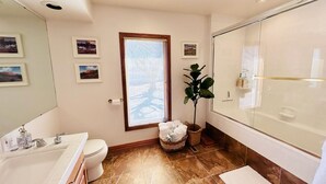 Et badeværelse med badekar, vask, toilet og et vindue med skodder.