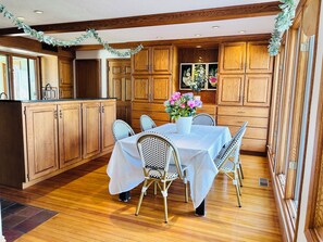 A wooden kitchen with a dining table set for four, surrounded by wicker chairs, and a potted plant with flowers on the table. - Boots & Class, where peaceful Iowa country living meets classy accommodations. (Harlan)