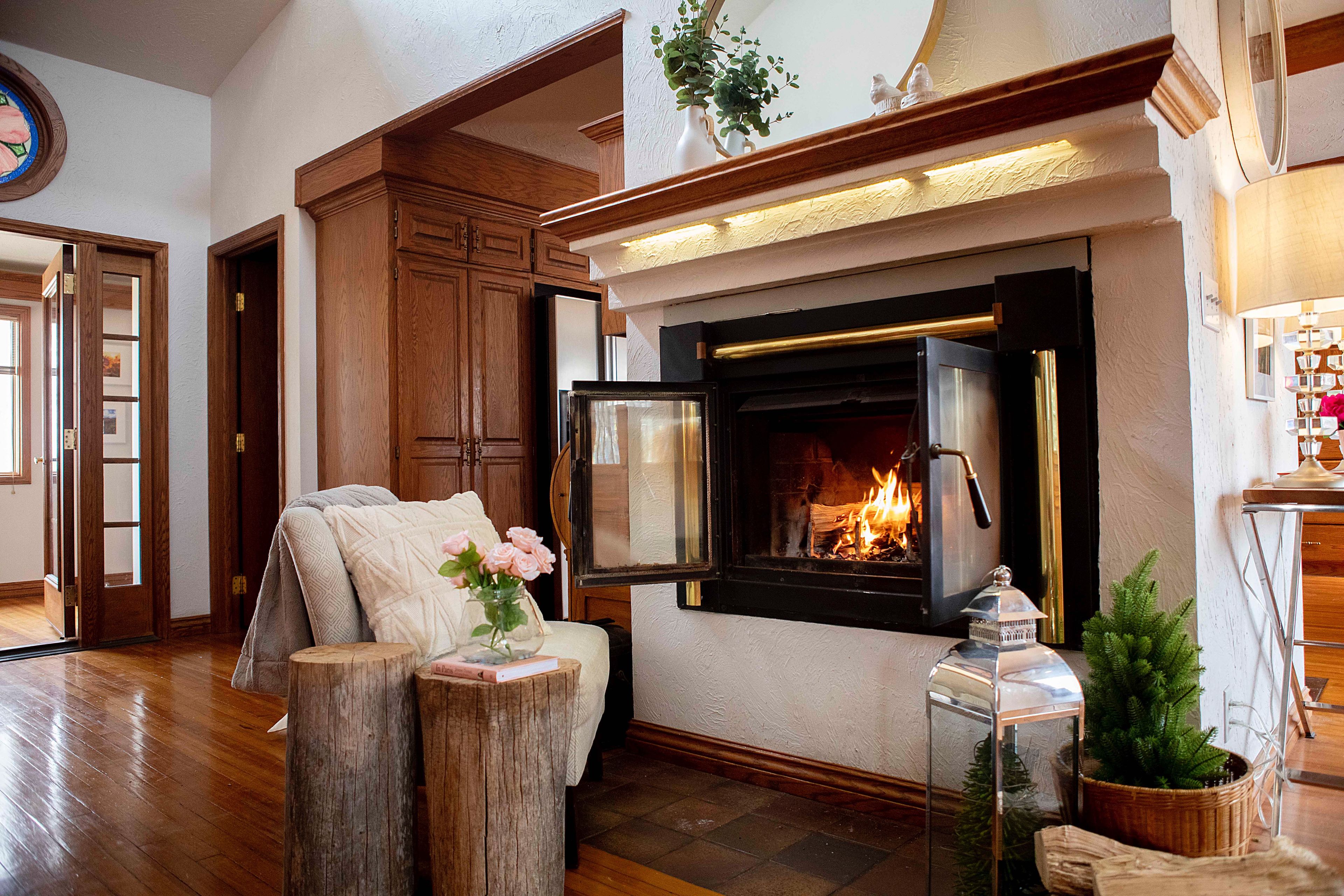 A cozy living room with a fireplace, wooden furniture, and a small Christmas tree.