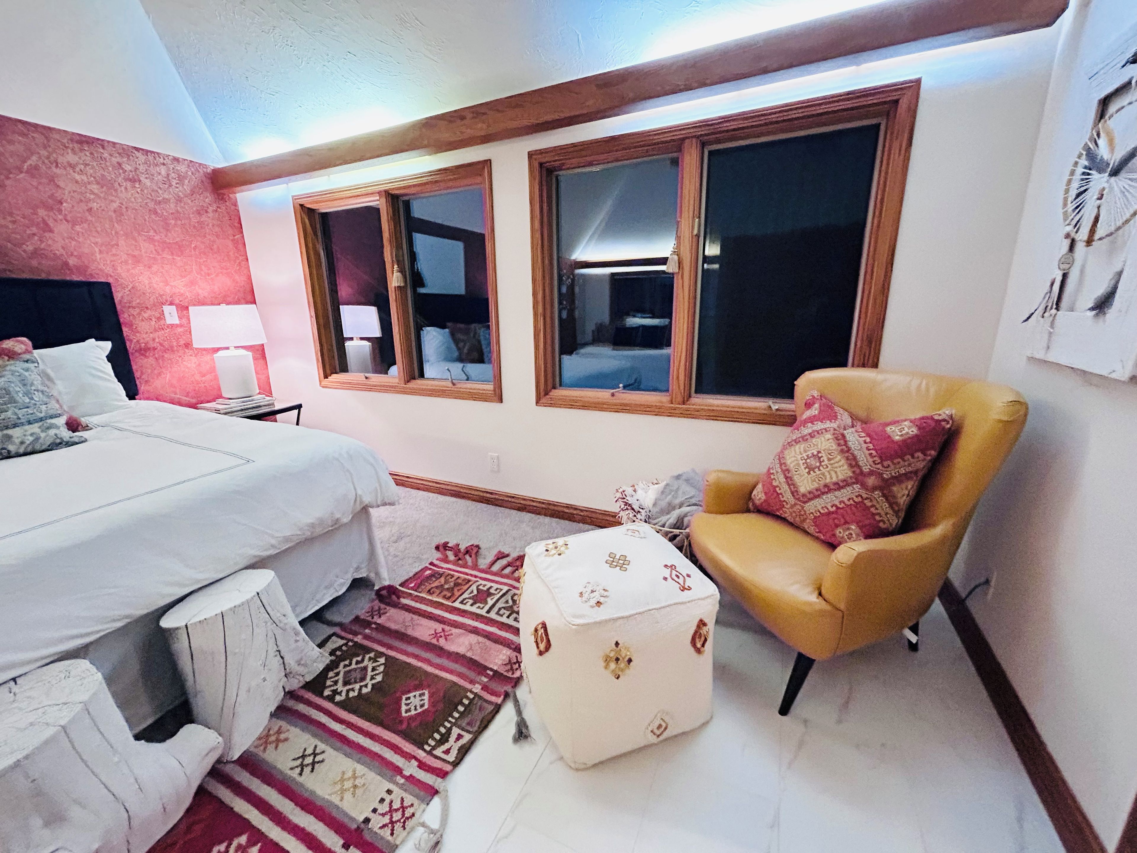 A bedroom with a bed, a chair, a nightstand, a lamp, and a window with a view.