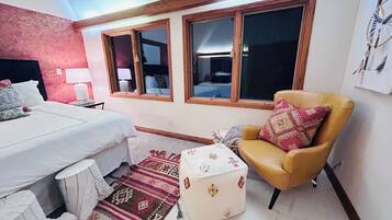 A bedroom with a bed, a chair, a nightstand, a lamp, and a window with a view.