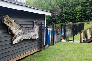 A building with a large wooden sign on the wall, a black metal fence, and a grassy yard. - Cozy Mt Snow Retreat  - Fireplace - Hot Tub -  Sauna (Dover)
