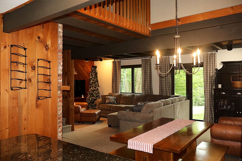 A cozy living room with a wooden interior, a fireplace, a Christmas tree, and a dining area with a table and benches.