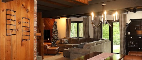 A cozy living room with a wooden interior, a fireplace, a Christmas tree, and a dining area with a table and benches.