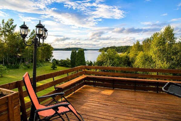 A wooden deck with a bench and a lamp post overlooking a lake.