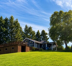 A modern house with a large deck, surrounded by a well-maintained lawn and tall trees.