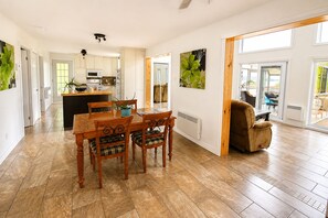 A spacious living area with a dining table, chairs, a sofa, and a view through a glass door to an outdoor patio.