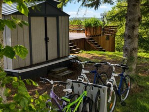 Un cobertizo de madera con escalones que lo llevan arriba, un aparcamiento para bicicletas con dos bicicletas y una escalera de madera.