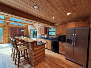A wooden cabin interior with a kitchen area featuring a refrigerator, stove, and sink. - Ski-in/Ski-out 9 bed log cabin on Pleasant Mountain with Moose Pond lake access (Bridgton)