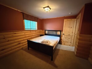 A bedroom with a wooden bed, a nightstand, a window with blinds, and a door. - Ski-in/Ski-out 9 bed log cabin on Pleasant Mountain with Moose Pond lake access (Bridgton)